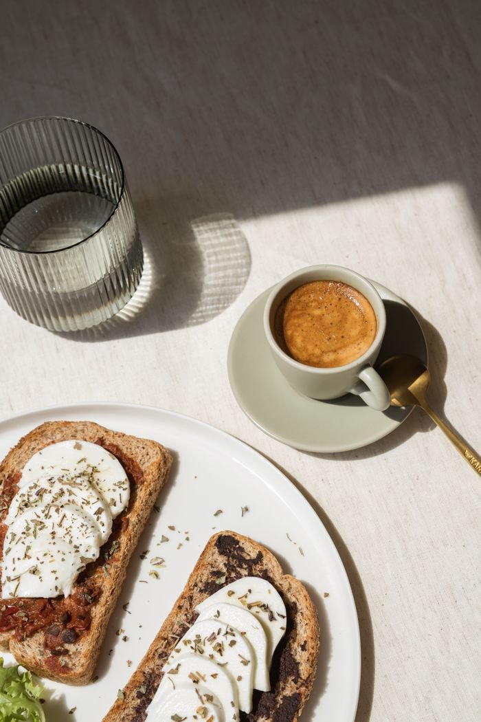 Top view of breakfast with toast, white cheese, and coffee in soft sunlight.